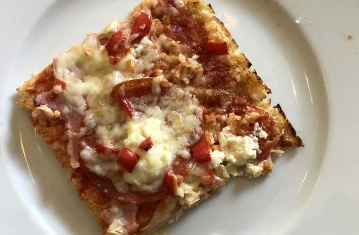 Ein Stück glutenfreie Blumenkohl-Pizza auf einem weißen Teller