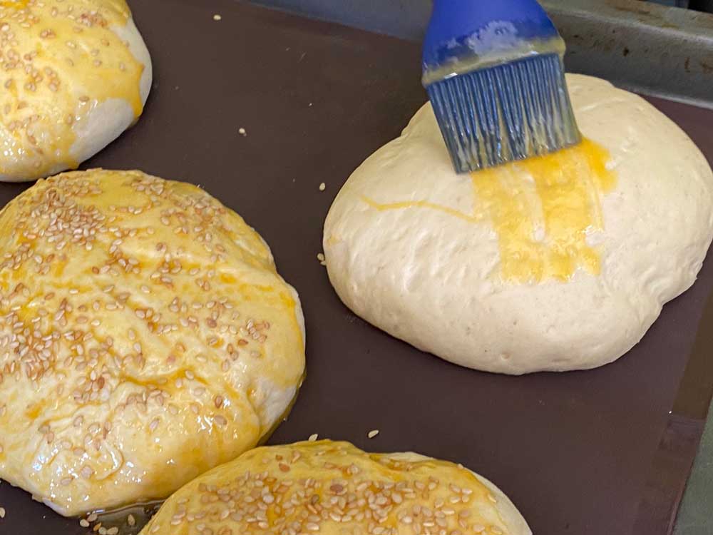 Glutenfreie Hamburger Brötchen werden mit Ei bepinselt